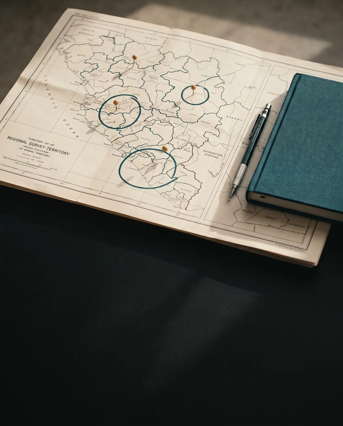 Une carte régionale dépliée, trois zones entourées à l'encre et repérées par des épingles